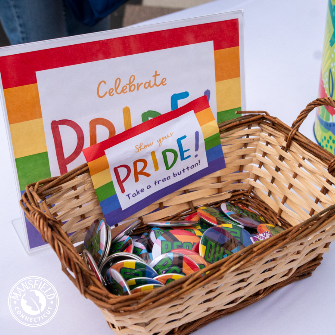 A basket of Pride pins with a sign encouraging folks to take a free pin