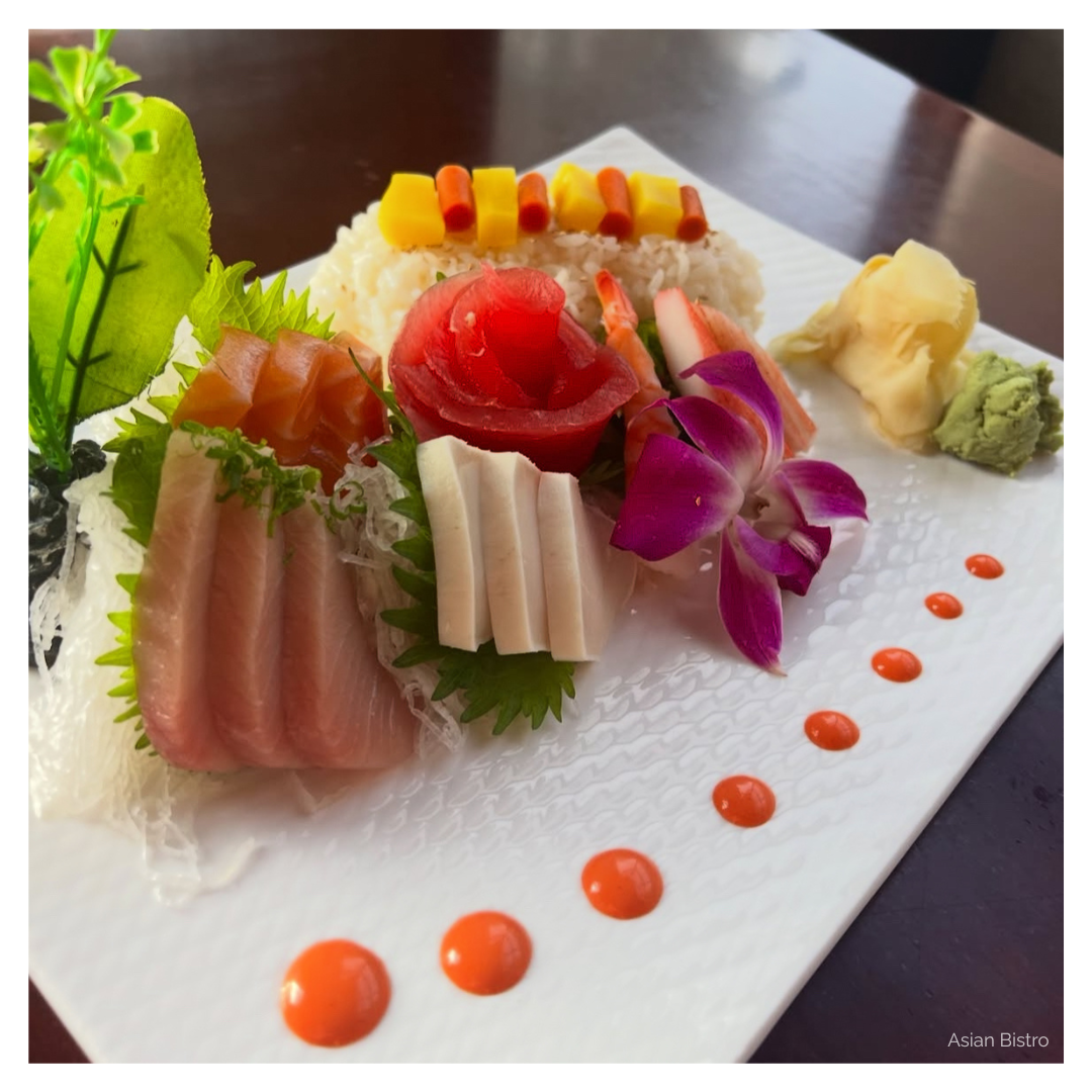 A plate full of sashimi and sushi is garnished with ginger, wasabi, and a tropical flower